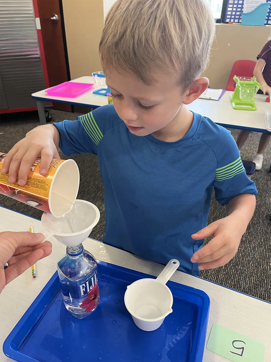 kindergarten-water-funnel-science-experiment Child performing water funnel science experiment with blue liquid and funnel apparatus