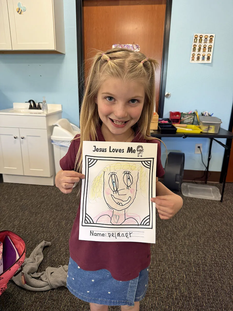 preschool-jesus-loves-me-bible-coloring-craft Child holding a colorful Jesus Loves Me Bible coloring craft